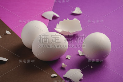 三个白色的鸡蛋与蛋壳碎片上的紫色，粉红色和棕色的颜色素净的最小的背景，角度观看，复活节快乐