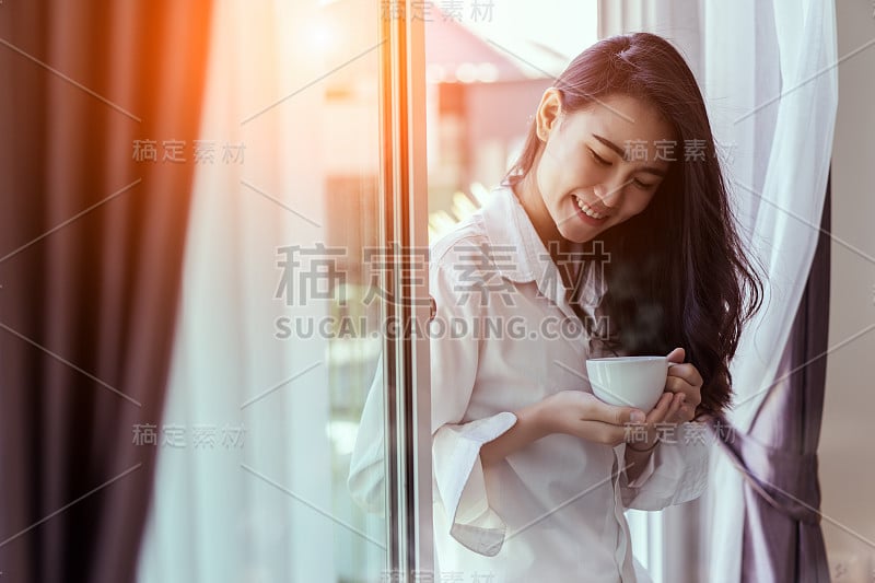 亚洲女人在早上喝咖啡在窗户卧室早餐新鲜开始一天幸福放松在家里健康的生活理念