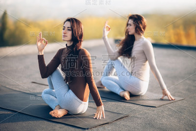 两个年轻的女人在户外屋顶上做着半身鱼的瑜伽体式