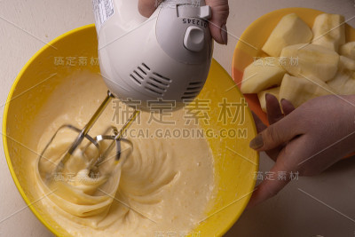 一位妇女在一个黄色的碗里用电动搅拌机搅拌馅饼的原料。