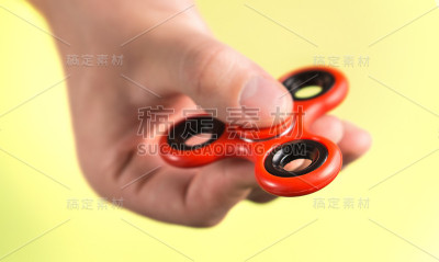 红色指尖陀螺之间的手指对淡黄色的背景。
