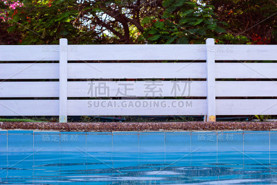花园白色木栅栏靠近游泳池边的放松空间在后院的背景图片