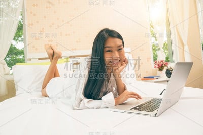 年轻的亚洲女性在床上用笔记本电脑看电影、工作或网上购物。