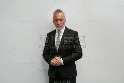 肖像的信心。成功成熟的商人在经典穿着看着相机，而站在灰色背景