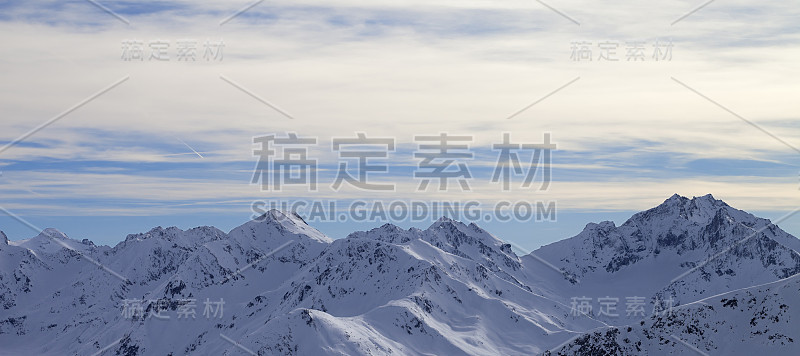 冬季高山多雪的山坡，傍晚阳光普照多云的天空