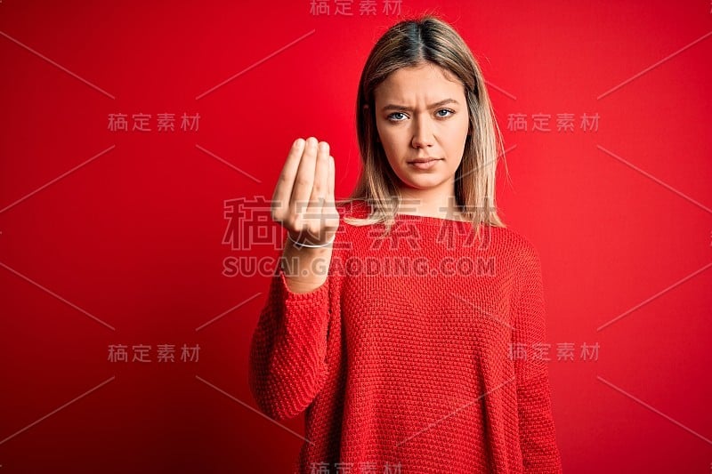 年轻美丽的金发女人穿着休闲毛衣在红色孤立的背景做意大利手势的手和手指自信的表情