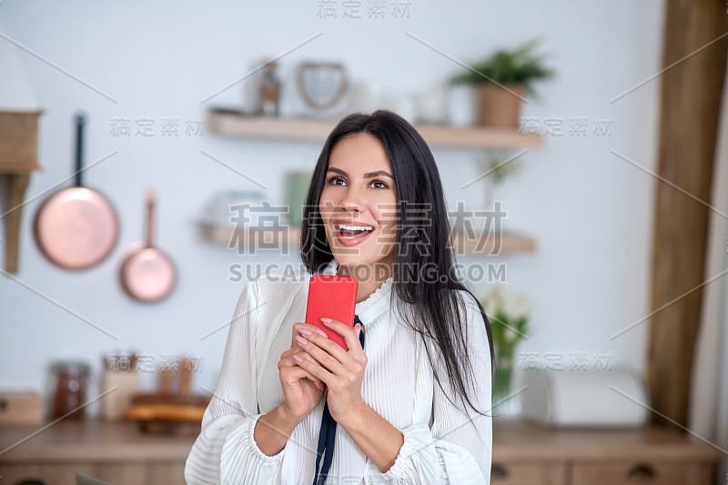 年轻女子拿着红色的智能手机，兴奋地微笑着