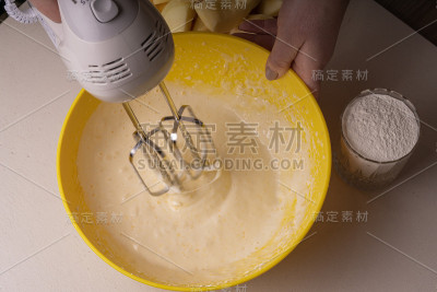 一位妇女在一个黄色的碗里用电动搅拌机搅拌馅饼的原料。