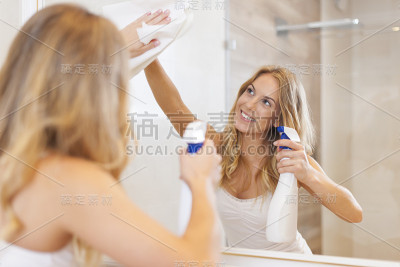 年轻的金发女郎在浴室里擦镜子