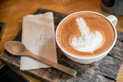 顶视图热咖啡卡布奇诺拿铁艺术在棕色陶瓷杯与木制勺子和纸巾在木制盘子