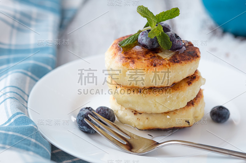 蓝莓白干酪煎饼盘，近景。健康美味的早餐，蜂蜜和浆果芝士蛋糕。传统的乌克兰菜肴白干酪煎饼配酸奶油。