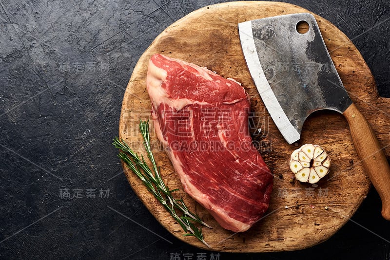 生鲜大理石肉黑安格斯牛排和切肉刀在木板上。黑色背景的肉，配上迷迭香和大蒜。副本的空间。前视图。