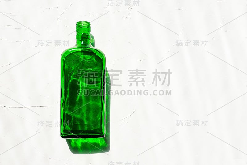 白色背景上的绿色瓶子。来自太阳的阴影。自然背景。俯视图，复制空间。