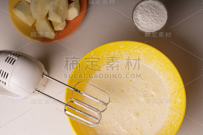 一位妇女在一个黄色的碗里用电动搅拌机搅拌馅饼的原料。