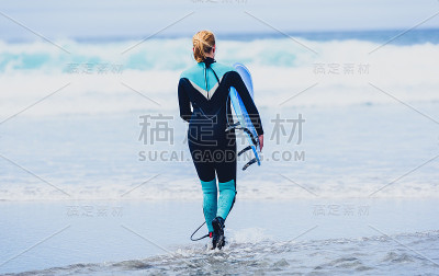 带着冲浪板的冲浪女正在边走边看海浪。