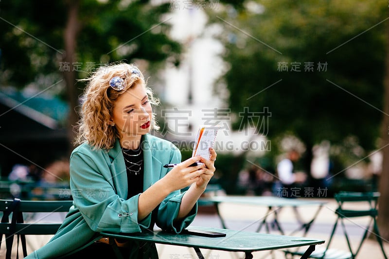 女人坐在桌子旁边，拿着笔和笔记本