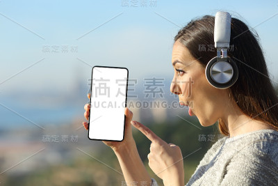 惊讶的女孩指着空白的智能手机屏幕，脸上充满了惊喜