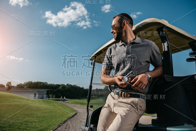 沉思的人与高尔夫球在手里看向别处，而站在高尔夫球车附近