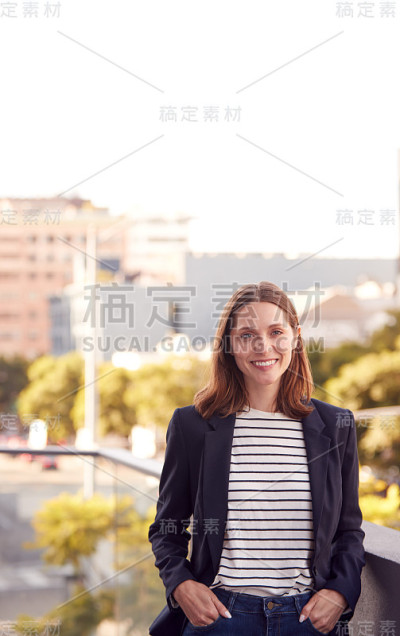 微笑的女商人站在办公楼外，城市天际线为背景