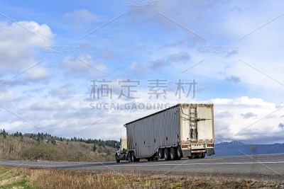 日驾驶室大钻机半挂车运输货物在有盖的波纹散货半挂车上行驶在自由的山路上