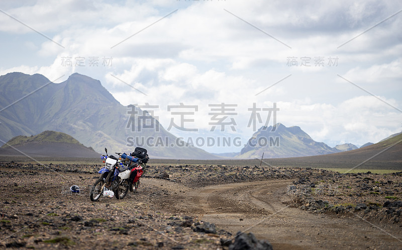 两辆摩托车站在被群山环绕的沙漠土路上，冰岛。越野旅行概念，耐力骑手装备，极端的生活方式