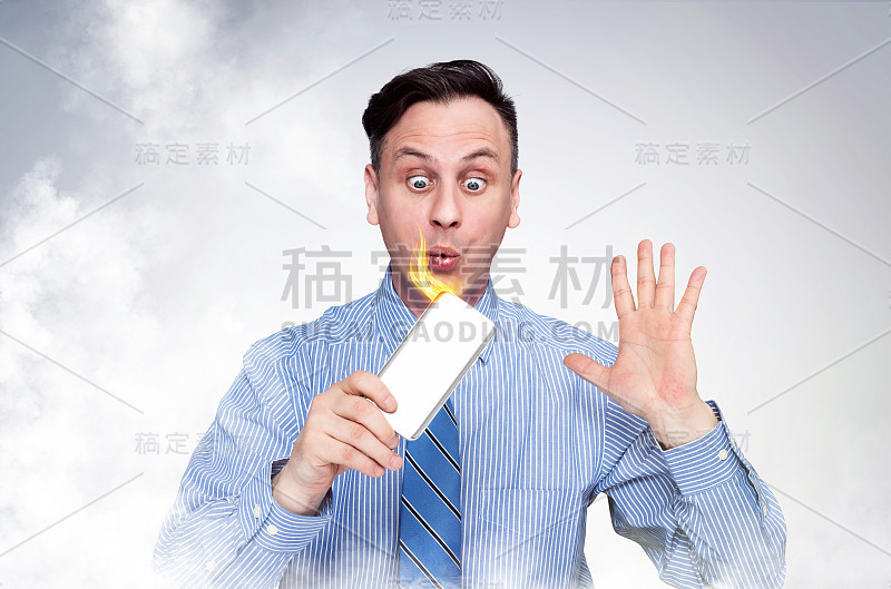 一名身穿衬衫打着领带的惊慌男子，试图扑灭手中燃烧的智能手机。移动设备火灾情况