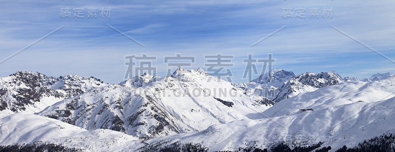 在冬季高山雪坡和蓝色阳光下多云的天空全景