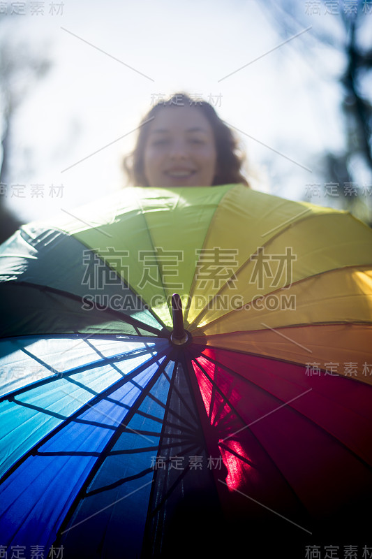 在一个阳光明媚的日子里，用许多颜色的伞背光的漂亮女人