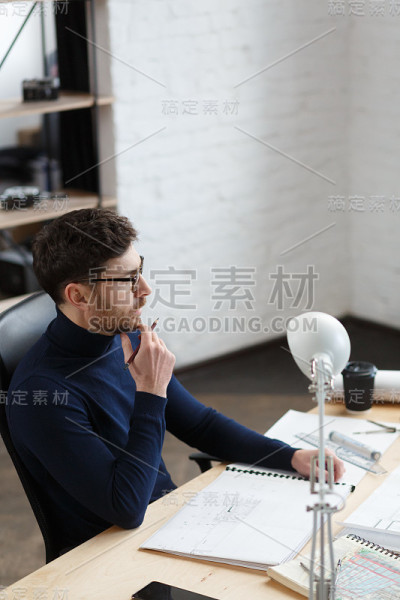 建筑师在办公室里设计蓝图。工程师检查建筑平面图，为建筑工程画草图。长着胡须的英俊男子坐在工作场所的肖