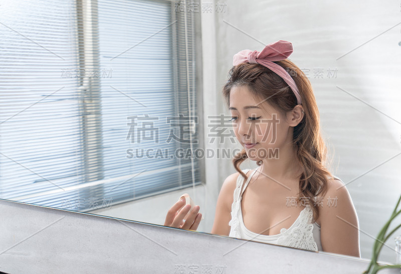 近距离的微笑女人化妆刷近脸和看镜子。亚洲美女