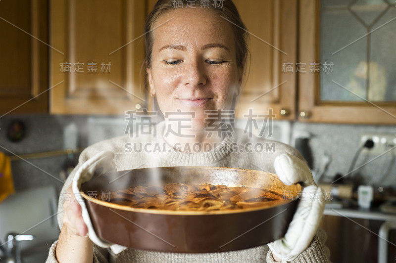 一个年轻女子拿着一个烤盘，上面放着一个现成的蛋糕