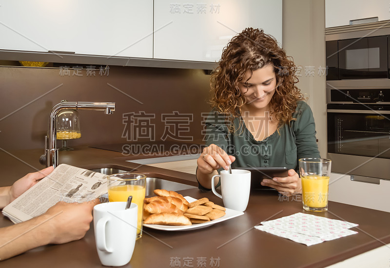 微笑的女孩吃早餐时用平板电脑看新闻