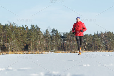 一个年轻人在冬天阳光明媚的森林里跑步