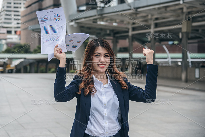 美丽的亚洲女人的肖像看起来快乐和信心是站着和拿着文件工作，而感觉与工作的成功。