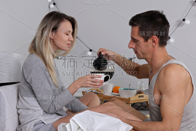 幸福的年轻夫妇吃浪漫的早餐，在床上喝咖啡。爱，关系，温柔，舒适，舒适的生活方式
