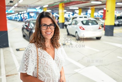 年轻女子自信地微笑在地下停车场周围的汽车和灯光