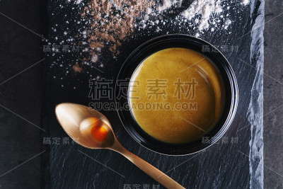 美丽的照片，金色的奶油护肤产品在一个大的优雅的黑色玻璃瓶附近的金色勺子与各种颜色的油滴在黑色的石头表