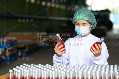 年轻女工戴着安全帽和医用口罩，在工厂里寻找和选择饮料