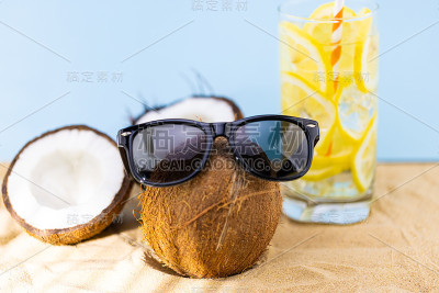 戴着太阳镜的时髦椰子和沙滩上的一杯柠檬水。暑假的概念