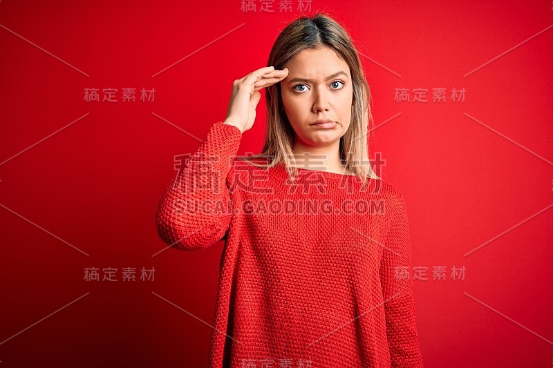 年轻美丽的金发女人穿着休闲毛衣在红色孤立的背景担心和强调一个问题与手的额头，紧张和焦虑的危机