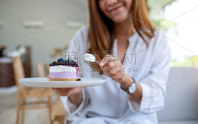 一个女人拿着一块蓝莓芝士蛋糕吃
