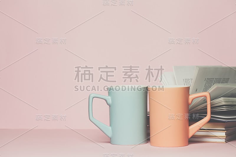 特写的两个杯子和一本书在粉红色的背景。为你的文本或设计复制空间