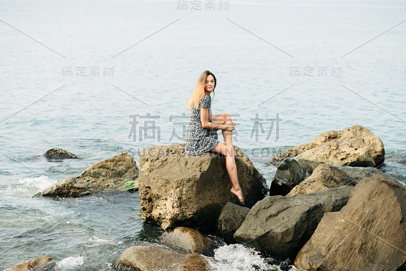 一个年轻美丽的女孩穿着大石头，风景如画的海边