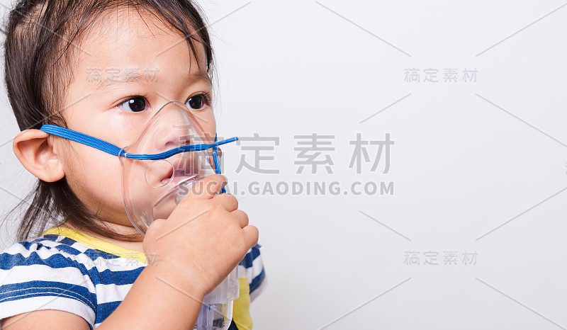 特写亚洲脸，小女婴生病了，她用蒸汽吸入器喷雾器面罩吸入自己的白色背景
