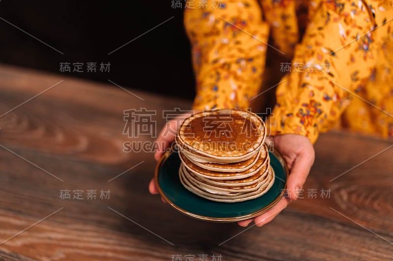 身着黄色连衣裙的女子手里拿着一个盛有蜂蜜煎饼的碟子。