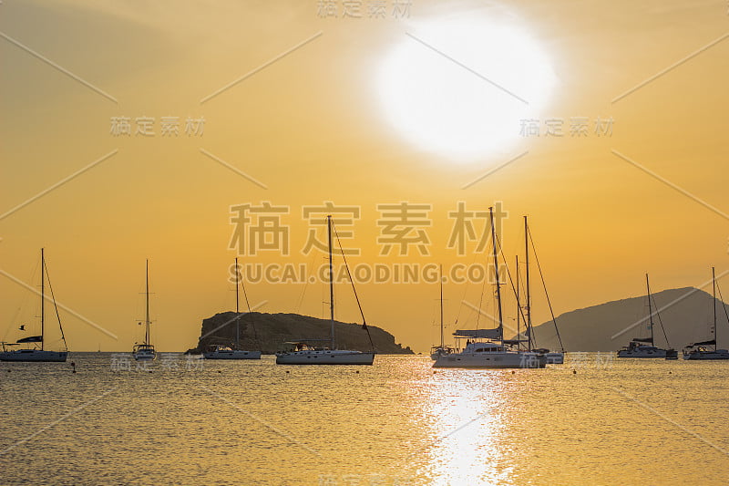 风景如画，雄伟豪华的地中海海湾海岸线风景，水上岩石悬崖和游艇的剪影在生动的橙色日落和天空背景