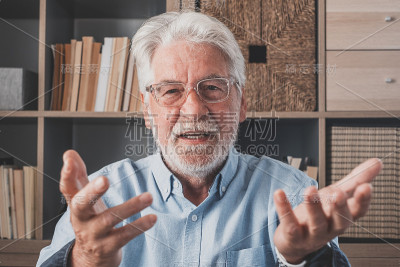 头像自信的老商人教练戴着眼镜看着相机和说话，导师演讲者举行在线课程，解释，坐在现代橱柜的木制办公桌