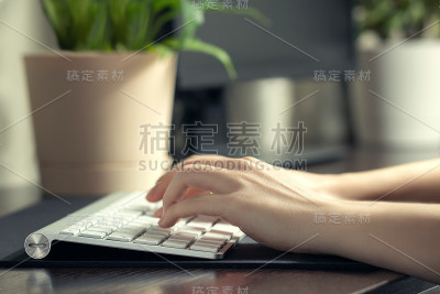 女孩在家里通过电脑工作。女性的手在键盘上打字