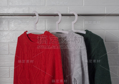 衣服挂在衣架上。红、绿、杂色的毛衣。时尚和风格，展示，商店，概念。白色砖墙，舒适和清洁，设计，舒适，