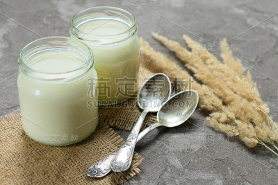灰色背景上放着两罐天然酸奶和小勺子。